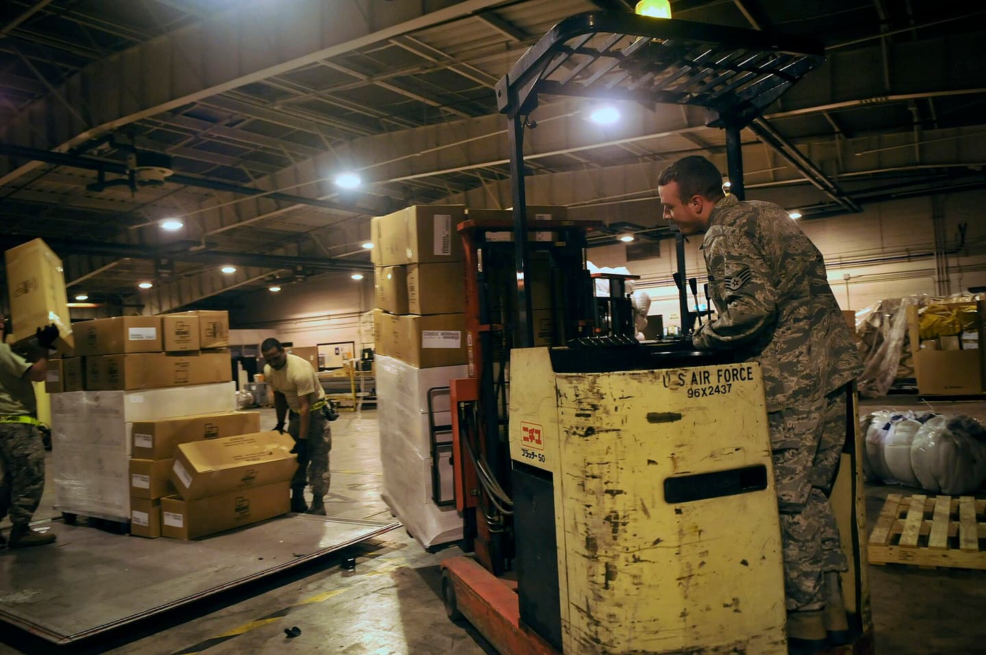 An airman moving palletised cargo on a forklift in a warehouse