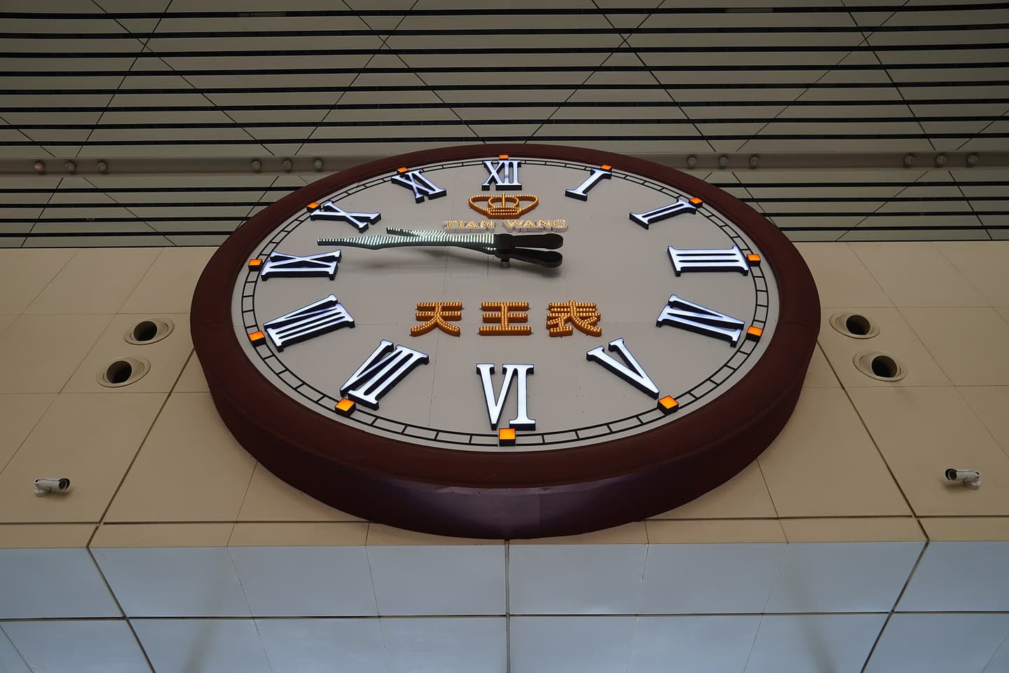 A large clock with Roman numerals in a railway station concourse